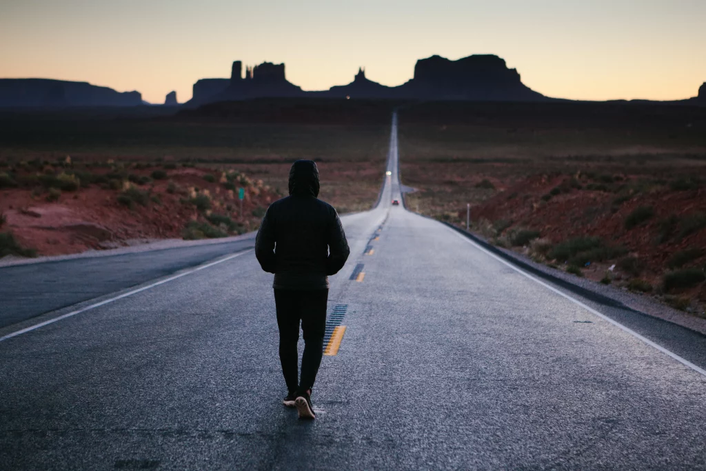 Pessoa andando sozinha por uma estrada ao entardecer. Ao fundo, canyons.